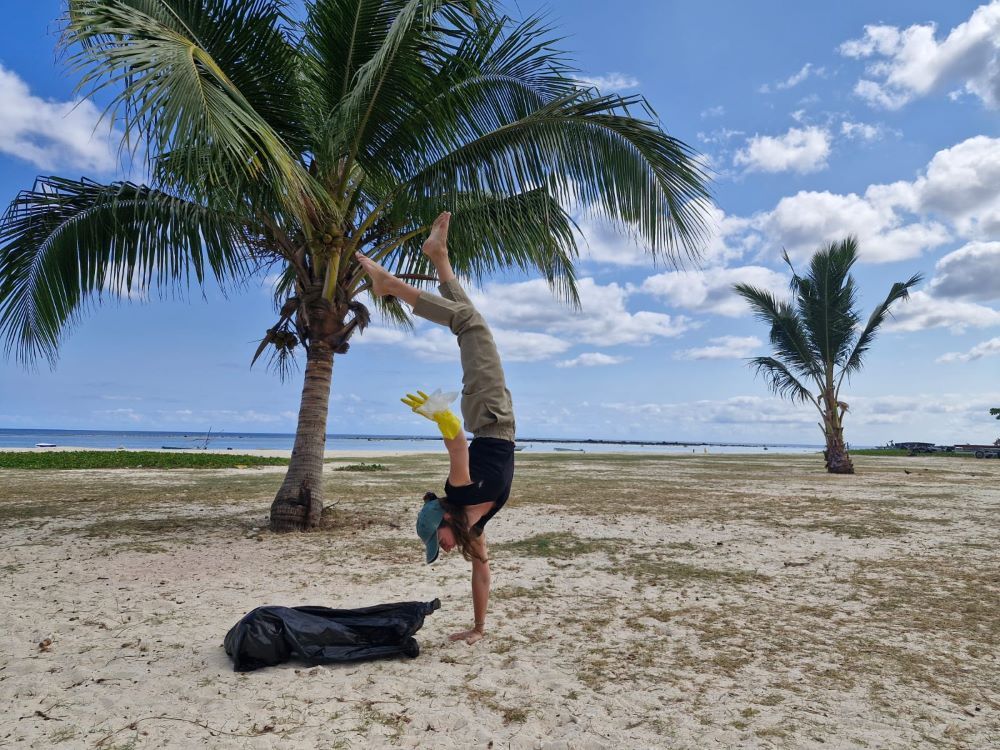 Photo fun sur la plage de Flic en Flac. Une membre de Mahé Technologies faisant l'équilibre sur une main, et tenant un sac plastique trouvé par terre dans l'autre main